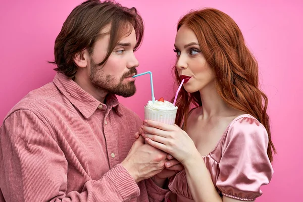Красивая кавказская пара наслаждается молочным коктейлем из одного стакана с двумя соломинками — стоковое фото