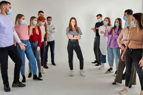 Grupo de personas sanas con máscaras médicas evitan el contacto con una pelirroja infectada de pie en el centro — Foto de Stock