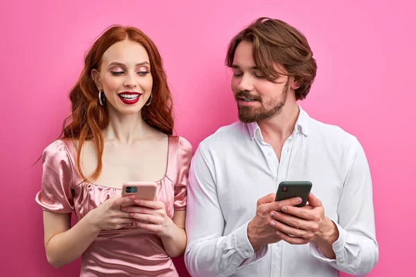 Kaukasische vrienden, man en vrouw gebruik smartphone geïsoleerd op roze achtergrond — Stockfoto