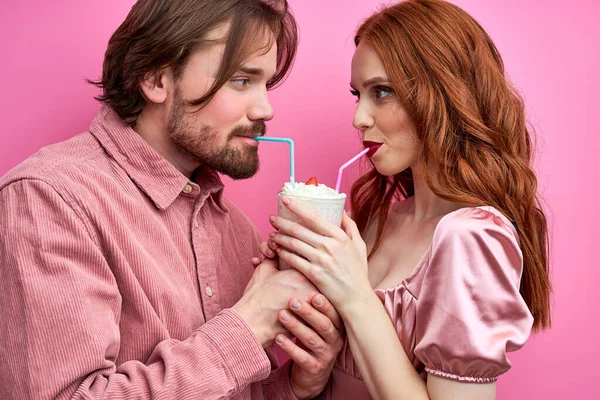 Очаровательная молодая пара наслаждается молочным коктейлем, выпивая из одного стакана с двумя соломинками — стоковое фото