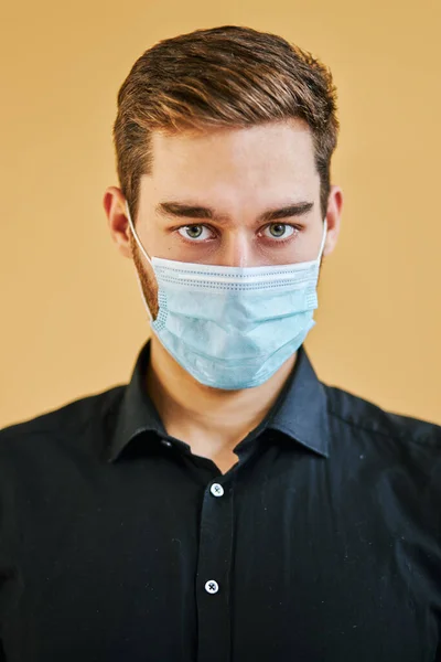 Bonito caucasiano homem em proteção médico máscara olhando para câmera seriamente — Fotografia de Stock
