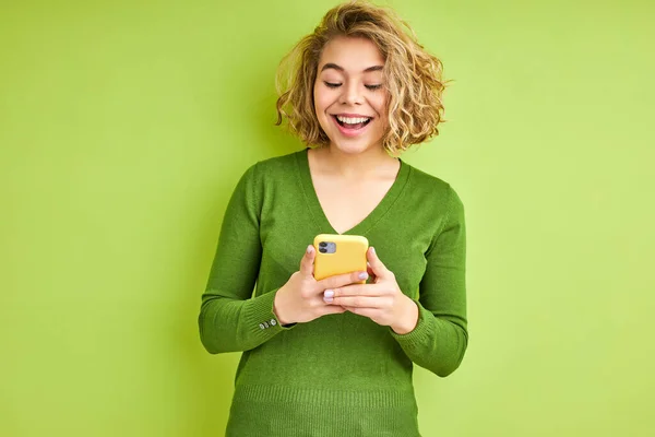 Portret van vrolijke opgewonden blonde krullende vrouw met behulp van smartphone — Stockfoto