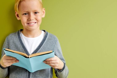 Zeki, neşeli, çalışkan, yeşil arka plan üzerine kitap okuyan, izole edilmiş bir okul çocuğu.