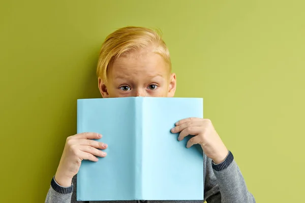 Портрет кавказского блондина, покрывающего лицо синей книгой — стоковое фото
