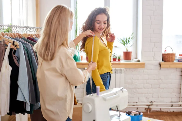 Joven diseñadora de moda femenina y bonita cliente que mide la longitud de la manga —  Fotos de Stock