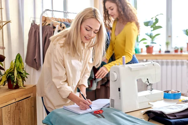 Diseñador de ropa caucásico toma notas mientras se prepara la sastrería en la sala de diseño, la creación de nuevo vestido —  Fotos de Stock