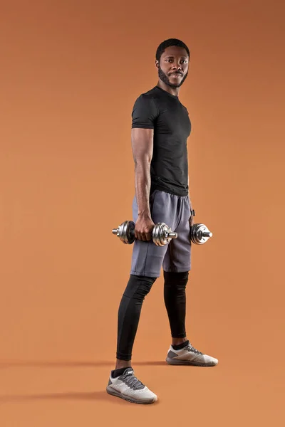 Guapo afro macho en deportivo uniforme va a entrenar con mancuernas —  Fotos de Stock