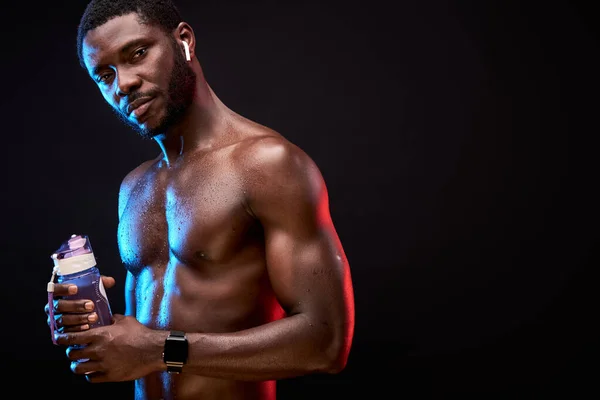 Retrato de atleta preto macho com nu torso segurando garrafa de água nas mãos — Fotografia de Stock