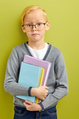 Ellerinde kitaplarla utangaç beyaz tenli inek çocuk, yeşil stüdyo arka planında izole edilmiş.