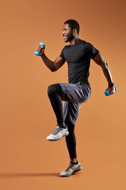 Sportif giyinen yakışıklı siyah afro erkek ağırlıkla egzersiz yapar, dambıl kullanır.