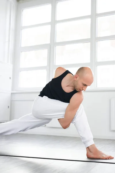 Йога. Молодой лысый человек, занимающийся йогой, изолирован на белом фоне в помещении — стоковое фото