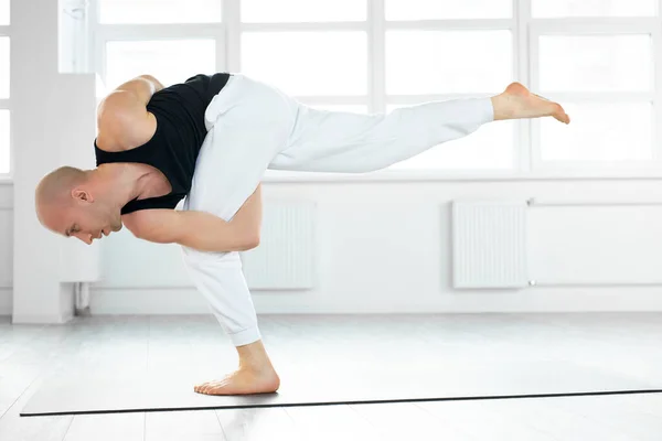 Спокойный кавказский йог с лысой головой сохраняет равновесие при выполнении осанки на одной ноге — стоковое фото