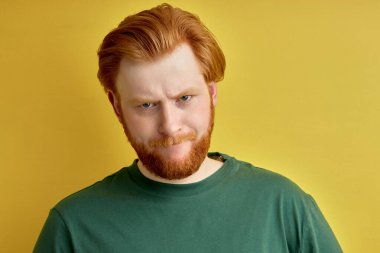 Tatmin olmamış kızıl saçlı erkek sarı arka planda izole edilmiş kameraya bakıyor.