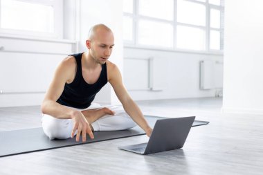 Yoga yapan, öğrencilere ders veren, dizüstü bilgisayarlı deneyimli bir Yogi erkeği.