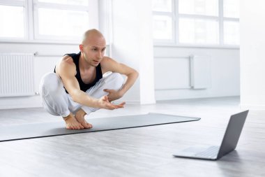 Genç kel adam internetteki talimatlarla kompleks yoga yapıyor.