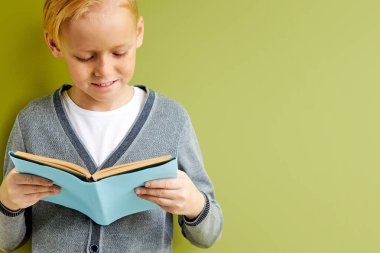 Okul yıllarında yeşil arka plana karşı büyüleyici kitaplar okuyan beyaz bir çocuk.