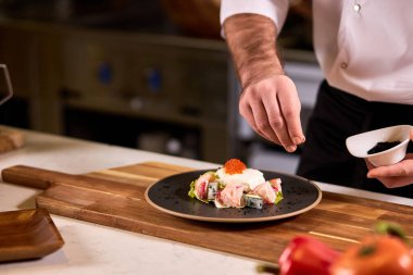 Genç aşçı, yemeğin tadını güzelleştirmek için biraz baharat ve sos ekler.