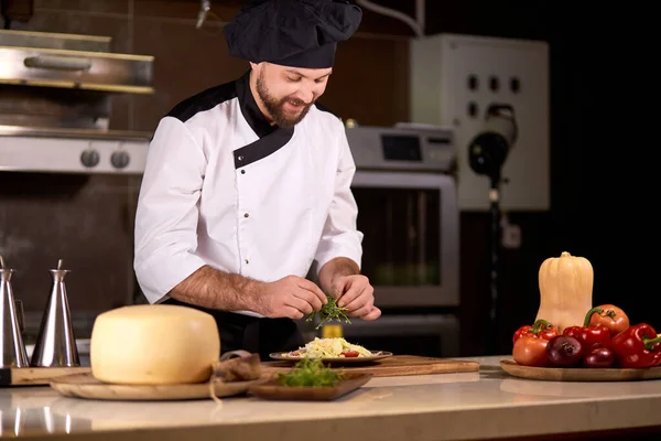 ヨーロッパのイタリア料理人は料理をきれいに仕上げ、いくつかの緑を加えます — ストック写真