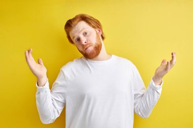 Yakışıklı kızıl saçlı beyaz adam izole edilmiş sarı arka planda günlük süveter giyiyor. Hiçbir şeyden habersiz ve kafası karışık.