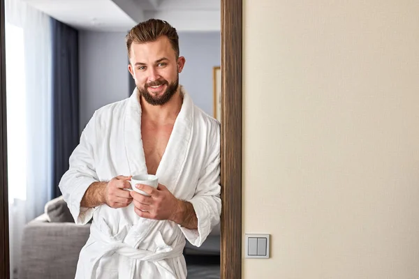 relaxed caucasian man in bathrobe spend holidays in hotel room, enjoy coffee in the morning