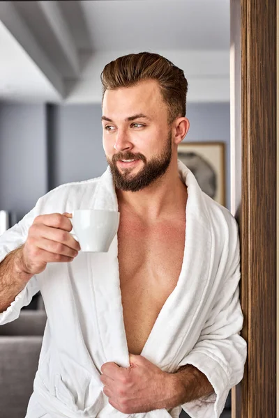 relaxed caucasian man in bathrobe spend holidays in hotel room, enjoy coffee in the morning