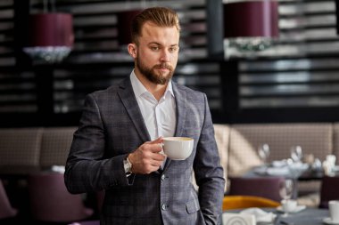 Yeni bir iş gününe başlıyorum. Yakışıklı genç adam restoranda bir fincan kahve tutuyor.