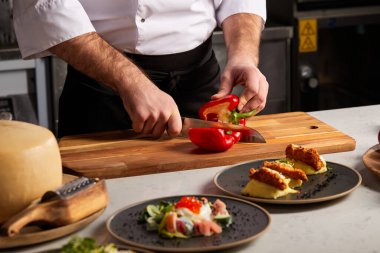 Yakın plan erkekler, restoranın mutfağında olgun kırmızı biberleri kesiyor.