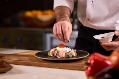 Oteldeki mutfak restoranında yemek pişiren profesyonel şef, salataya baharat ekliyor.