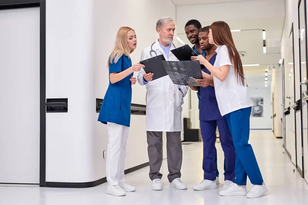 Csoportkép fiatal orvosokról beszélgetés közben vezető magabiztos orvossal a kórházi folyosón — Stock Fotó