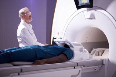 Erkek hasta MRI makinesinde yalan söylerken yaşlı profesyonel doktor ameliyat ediyor.