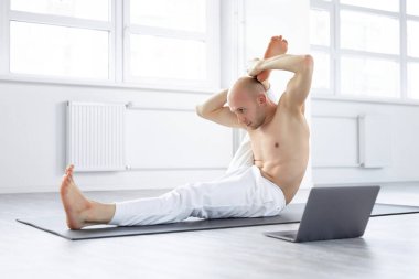 Kel, beyaz, üstsüz yogi adam laptopta egzersiz yapıyor.