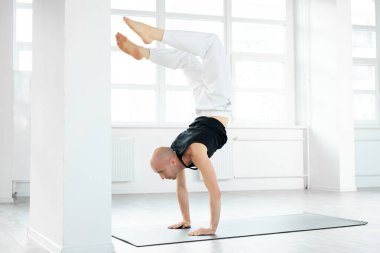 Parlak stüdyo odasında akrep yogası yapan deneyimli bir Yogi adamı.