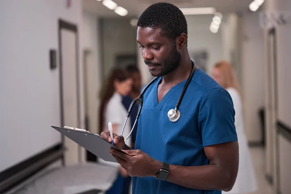 신뢰할 만 한 아프리카 계 미국인 의사 가 병원에서 클립보드를 들고 있는 푸른 의학 대학 에서 — 스톡 사진
