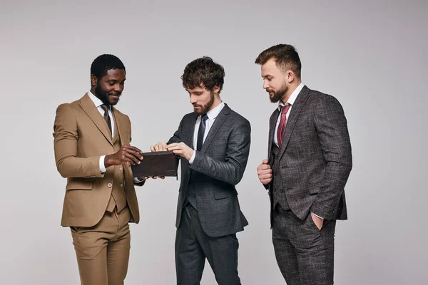 Jóvenes hombres de negocios diversos se paran mirando el bolso discutiendo dinero —  Fotos de Stock