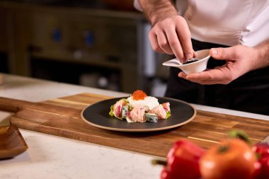 Oteldeki mutfak restoranında yemek pişiren profesyonel şef, salataya baharat ekliyor.