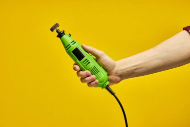 close-up Power tool. Green Die grinder in hands isolated on yellow background clipart