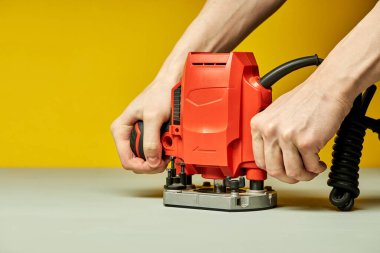 Tanımlanamayan bir erkeğin sarı arka planda elektrikli testereyi açması