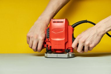 Kırpılmış erkek, sarı arka planda elektrikli testereyi açıyor.