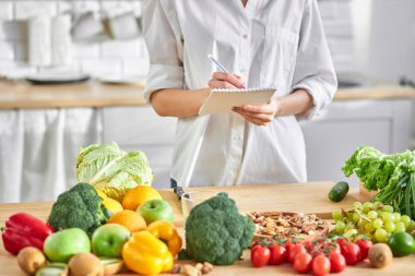 Kesilmiş kadın beslenme uzmanı mutfakta deftere yazıyor.