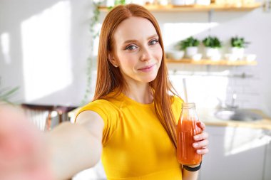 Çekici kızıl saçlı yemek blogcusu kadın mutfakta el yapımı meyve suyu içiyor.