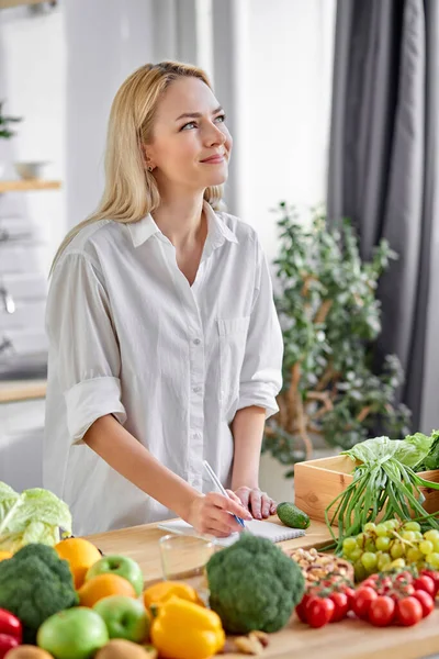 Woman writing diet plan on table and using vegetables. Sport trainer. Lifestyle.