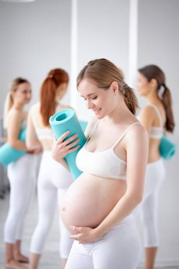 Koca göbekli çekici bir kadın bebek bekliyor, fitness stüdyosunda poz veriyor.