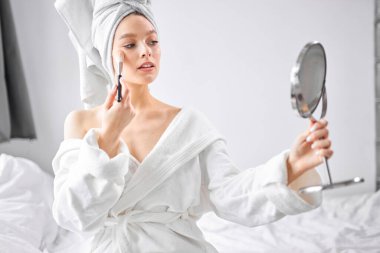 Beyaz aynaya sarılı bir kadın, dairede makyaj yapıyor.