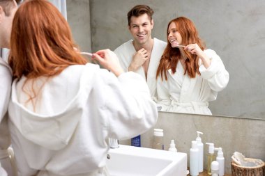 Birlikte sabah görevleri. Modern tasarlanmış banyoda aynanın önünde duran neşeli, evli bir çift.