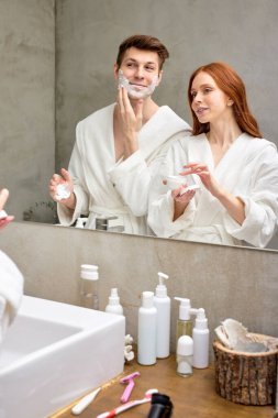 Bornozlu genç çift, sabahları banyoda birlikte geçirmeyi seviyor.