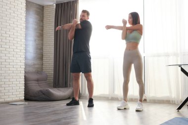 formda genç bir çift evde egzersiz yapıyor, kollarını uzatıyorlar ve pilates yapıyorlar.