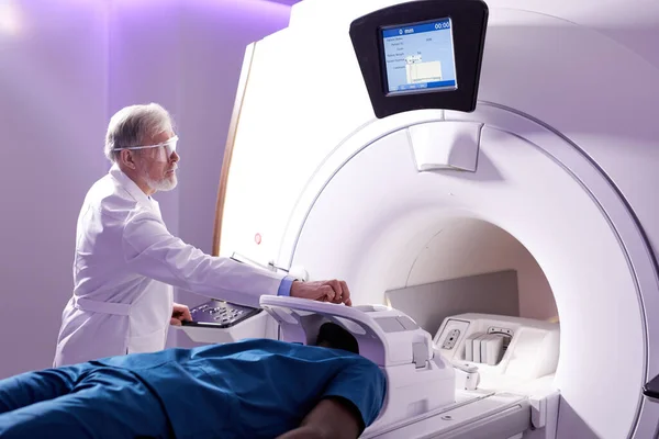 Male Patient Lying On MRI Machine While Elderly professional Doctor Operating It