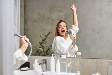 Bornozlu beyaz kadın banyoda eğleniyor, şarkı söylüyor.