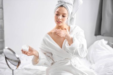 Havlu ve bornoz giymiş güzel bir kadın. Sabahları vücuduna krem sürüyor.