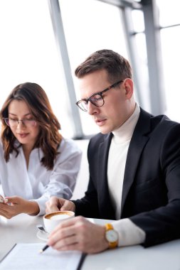 Gözlüklü bir iş adamı iş arkadaşını dinlerken oturup not alır.